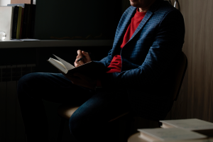 A foto está focada em um homem com um livro e uma caneta na mão.