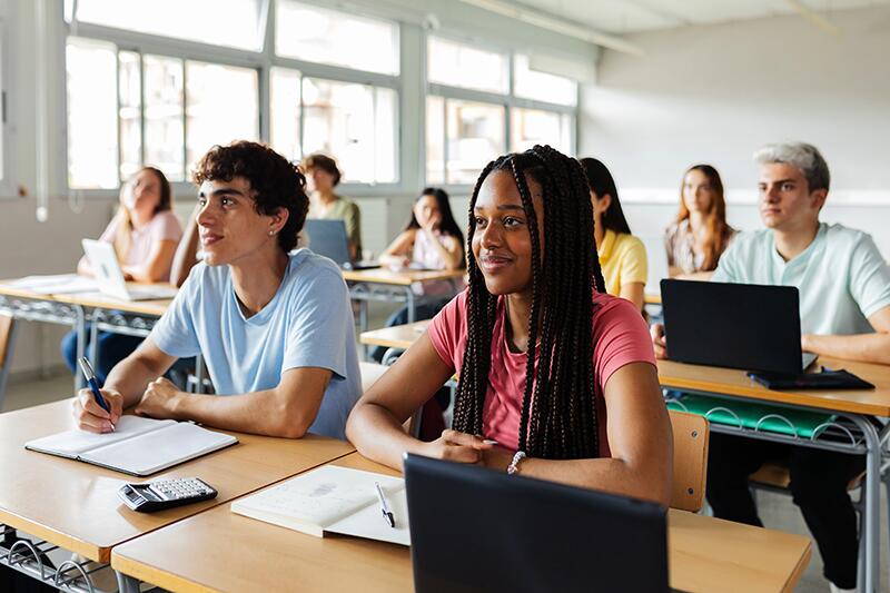 Jovens sentados em carteiras aparentemente prestando atenção na aula.