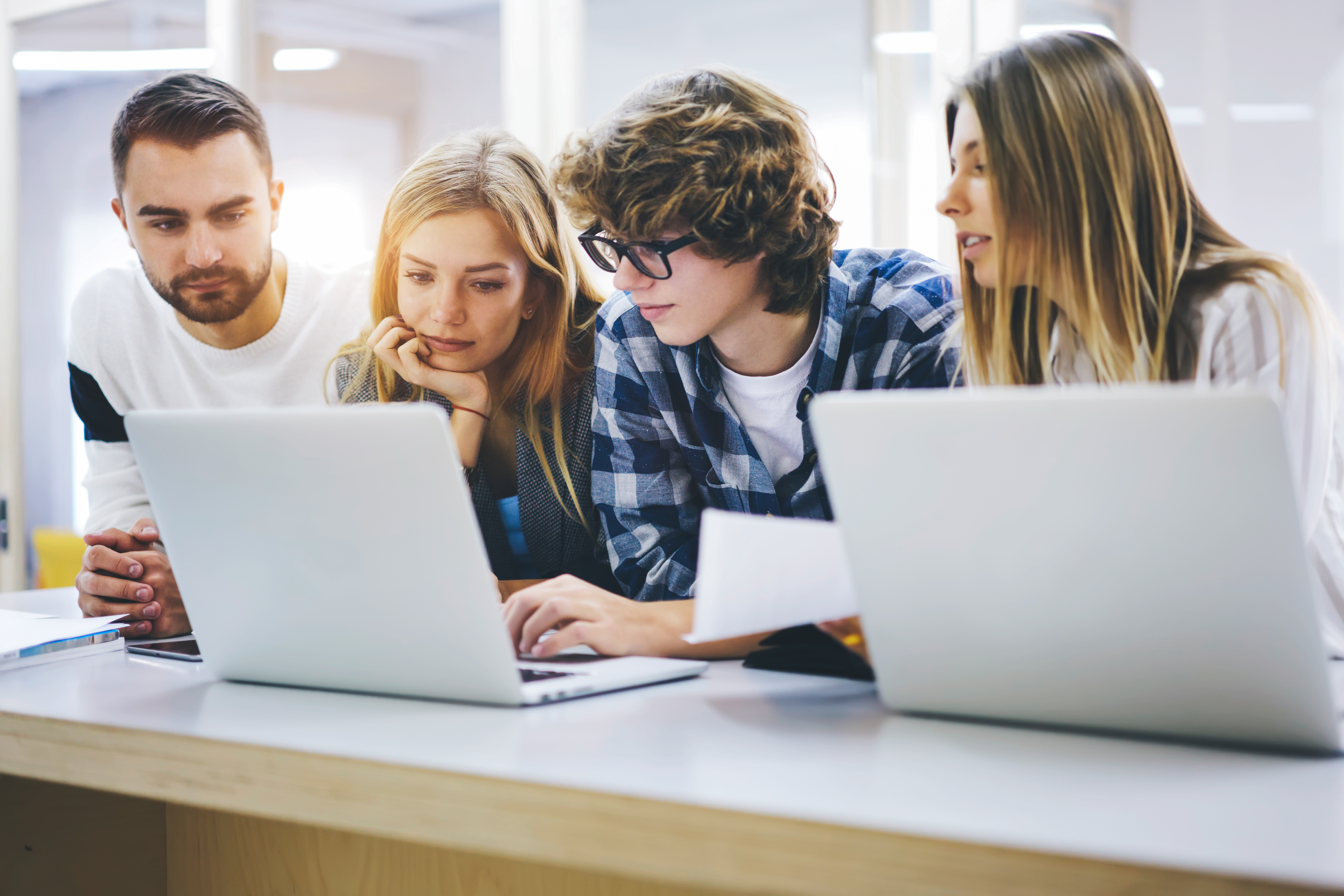 Grupo de jovens estudantes trabalhando juntos em computadores portáteis em sala de aula, colaborando em um projeto acadêmico.