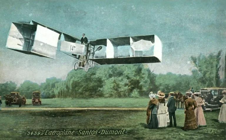 Reprodução da antiga aeronave Santos-Dumont, um avião histórico que simboliza pioneirismo na aviação, voando sob um céu azul, com um grupo de pessoas observando ao chão.