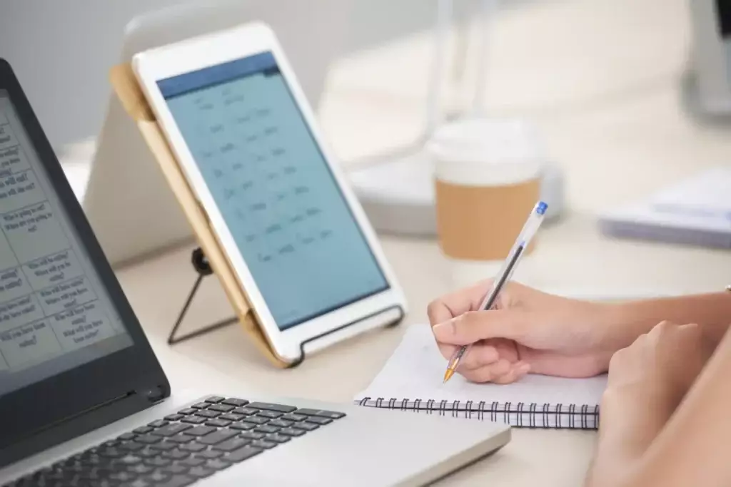 Pessoa estudando com laptop, tablet e caderno na mesa, ambiente de escritório ou estudo, foco em tecnologia e aprendizado. Already