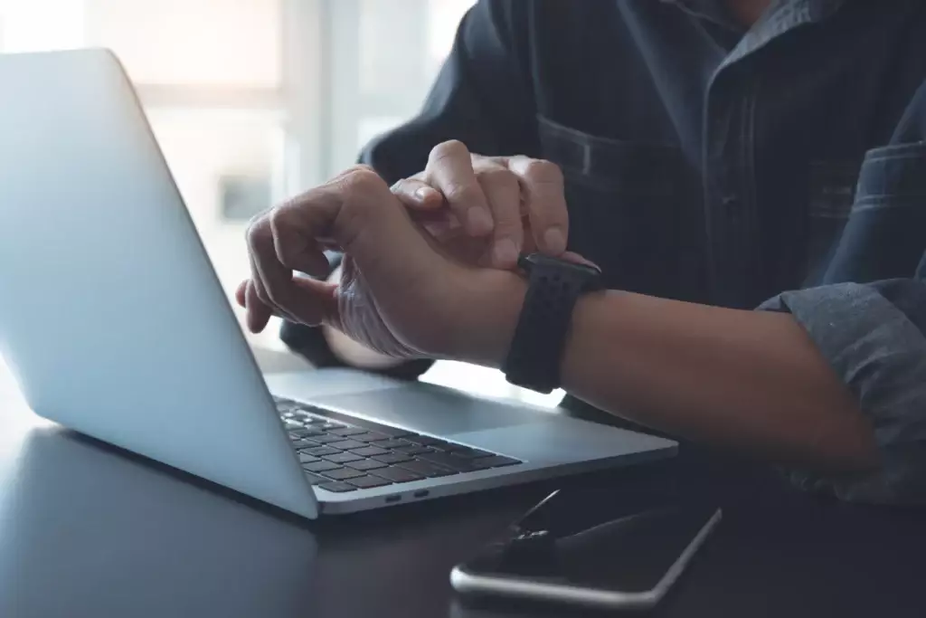 Pessoa verificando o smartwatch ao lado de um laptop em um ambiente de trabalho, simbolizando tecnologia, produtividade e monitoramento pessoal, contra o tempo ocioso