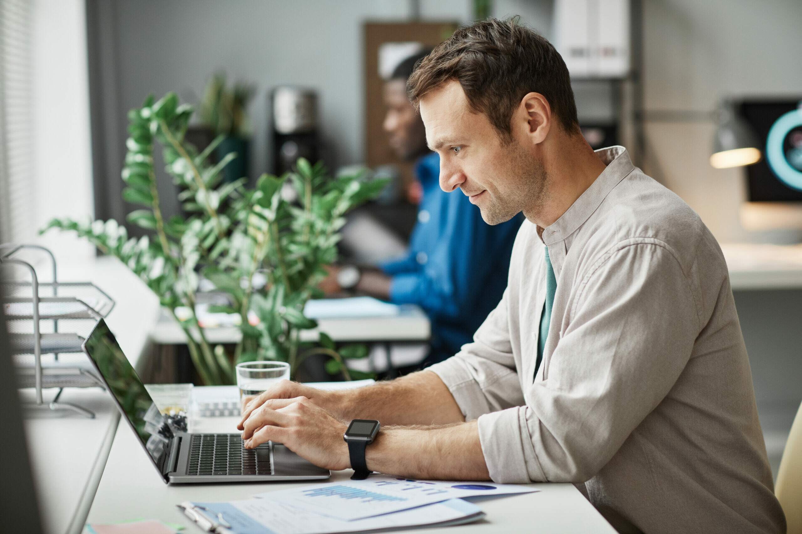 Homem sorridente usando notebook no escritório, representando profissional revisando seu perfil profissional e currículo