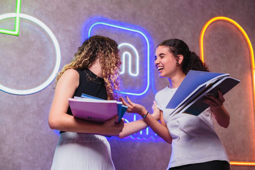 Jovens estudantes conversando e segurando materiais de estudo, representando oportunidades de aprendizagem e desenvolvimento profissional para jovem aprendiz.