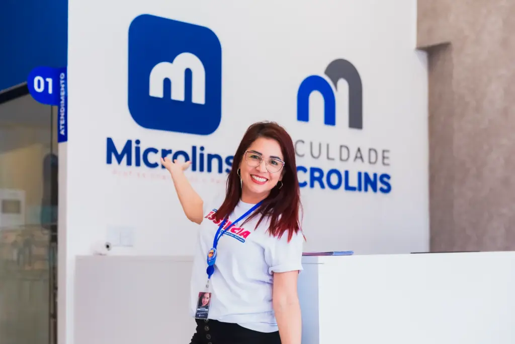Consultora Microlins sorrindo na recepção da unidade, representando 
o suporte profissional oferecido pelos cursos para quem busca 
se qualificar e melhorar o objetivo para currículo