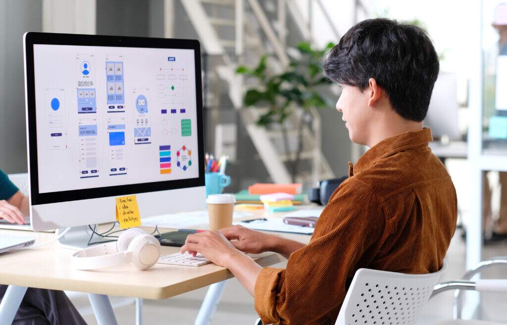 : Jovem estudando curso de web design no computador, aprendendo design de interfaces e criação de sites.