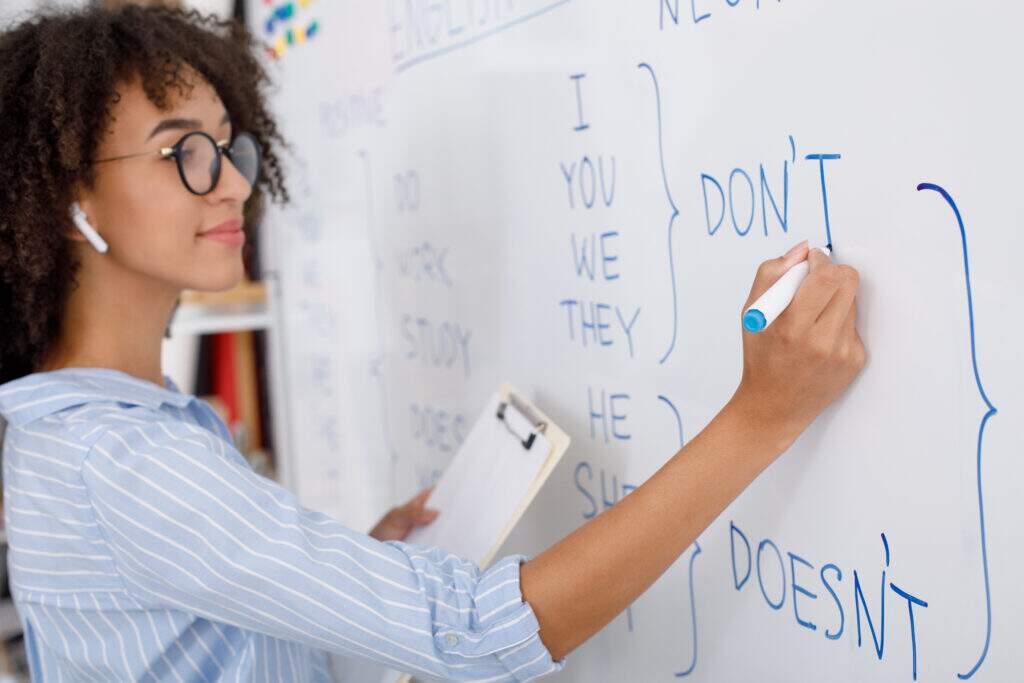 Jovem aprendendo inglês do zero em casa, com caderno de anotações, fones de ouvido e aplicativo de idiomas aberto no celular.