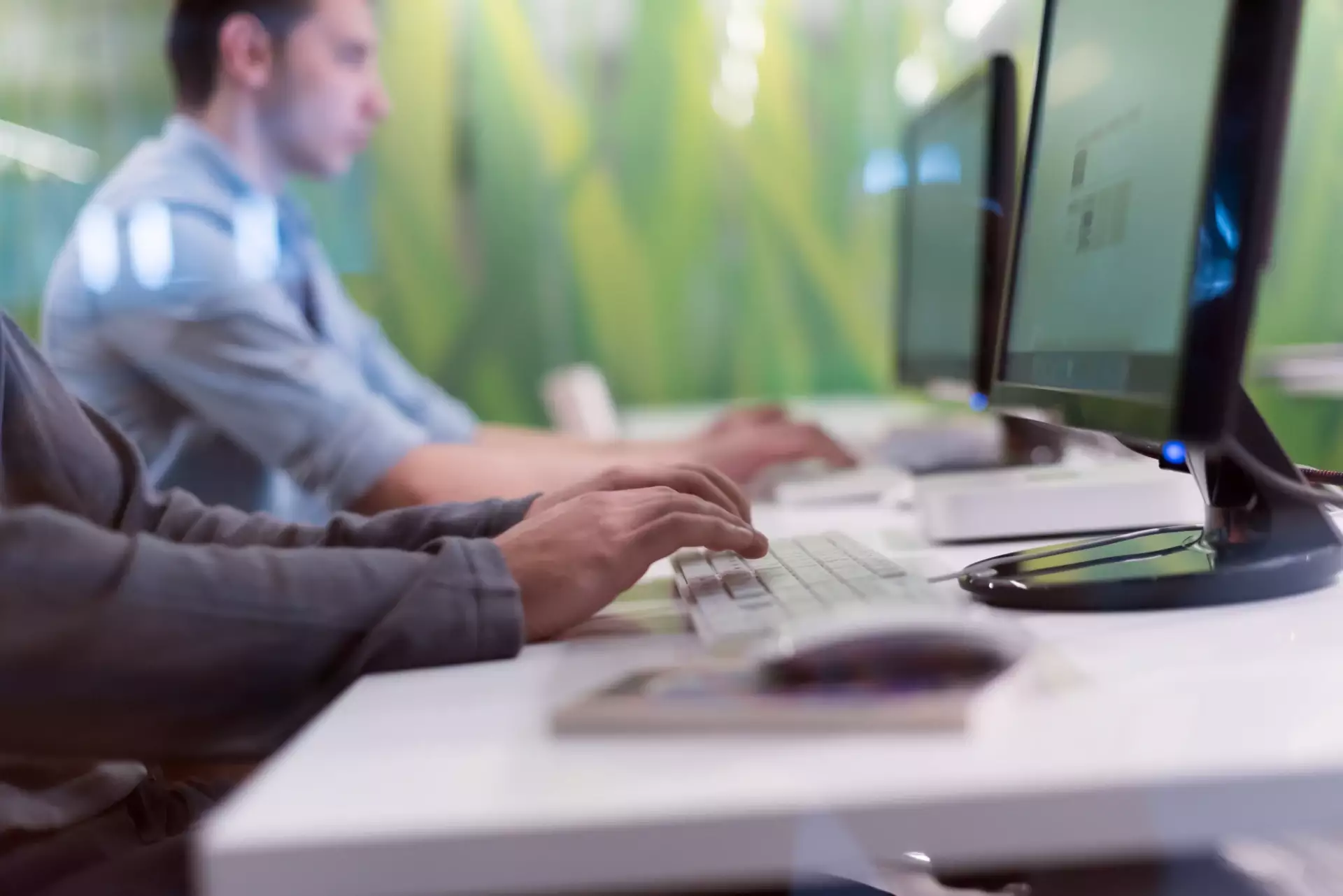 Pessoa usando computador em escritório, trabalhando com teclado e monitor enquanto realiza tarefas digitais. Ideias de noções de informática para produtividade